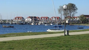 A marina with boats docked, a grassy area, and a row of houses with red roofs. - Modernes Ferienhaus mit Garten in Kagsdorf (Bastorf)