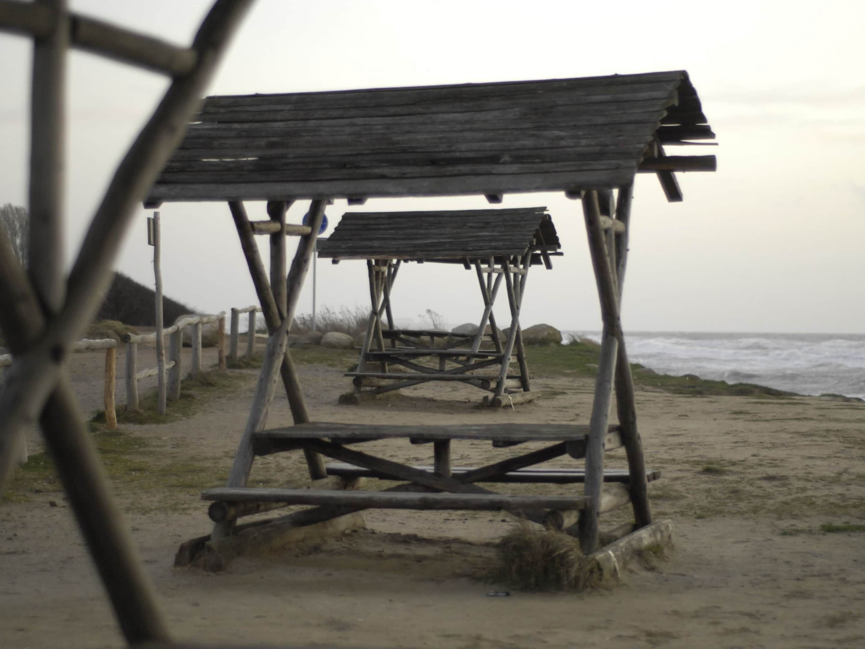 Een strand met houten constructies, waarschijnlijk strandhutten, en een zandpad dat naar de zee leidt.