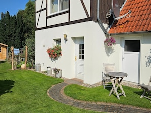 A white building with a red-tiled roof, a small garden with a paved path, and outdoor furniture. - Modernes Ferienhaus mit Garten in Kagsdorf (Bastorf)