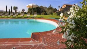 A swimming pool with a curved edge, surrounded by a brick deck. There are lounge chairs and a white umbrella in the background. - Agriturismo near Cortona with Spacious Garden & Swimming Pool (Cortona)
