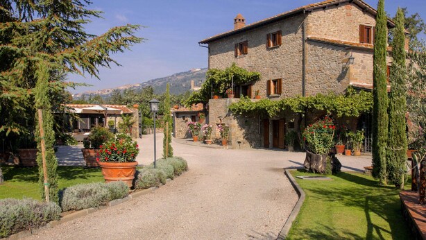 A stone building with a gravel driveway, surrounded by potted plants and greenery. - Agriturismo near Cortona with Spacious Garden & Swimming Pool (Cortona)