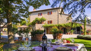 An outdoor dining area with a stone building in the background, a table set with plates, glasses, and a bottle of wine. - Agriturismo near Cortona with Spacious Garden & Swimming Pool (Cortona)