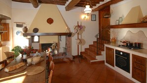 A rustic kitchen with a brick fireplace, wooden beams, and a dining area with a table set for two. - Agriturismo near Cortona with Spacious Garden & Swimming Pool (Cortona)