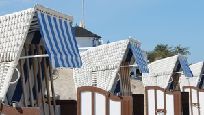 Een rij strandhutten met gestreepte luifels, houten deuren en een zandstrand op de achtergrond.