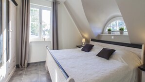 Een slaapkamer met een bed, nachtkastje, raam en gordijnen.