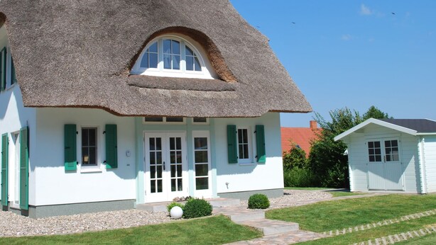 Een traditioneel huis met rieten dak, witte muren en groene luiken.