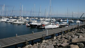 Een jachthaven met verschillende boten afgemeerd, een houten steiger en een rotsachtige kustlijn.