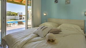 A bedroom with a bed, pillows, and a hat on the bed. There is a window with a view of a pool and outdoor furniture.
