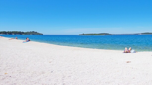 A beach with clear blue water and a sandy shore.