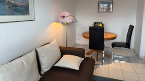 A living room with a brown sofa, a round wooden table with two chairs, a floor lamp, and a framed picture on the wall. - Cozy Apartment in Zingst Germany near Beach (Zingst)