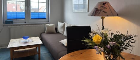 Un salon avec une table basse en bois, un canapé, une lampe et une fenêtre avec des stores.