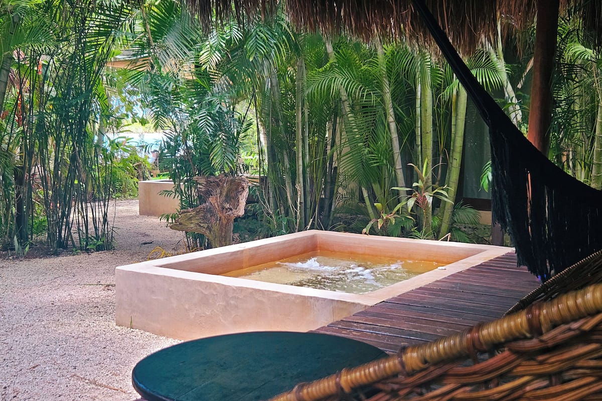 A spa area with a rectangular hot tub, a wicker chair, and lush tropical vegetation.