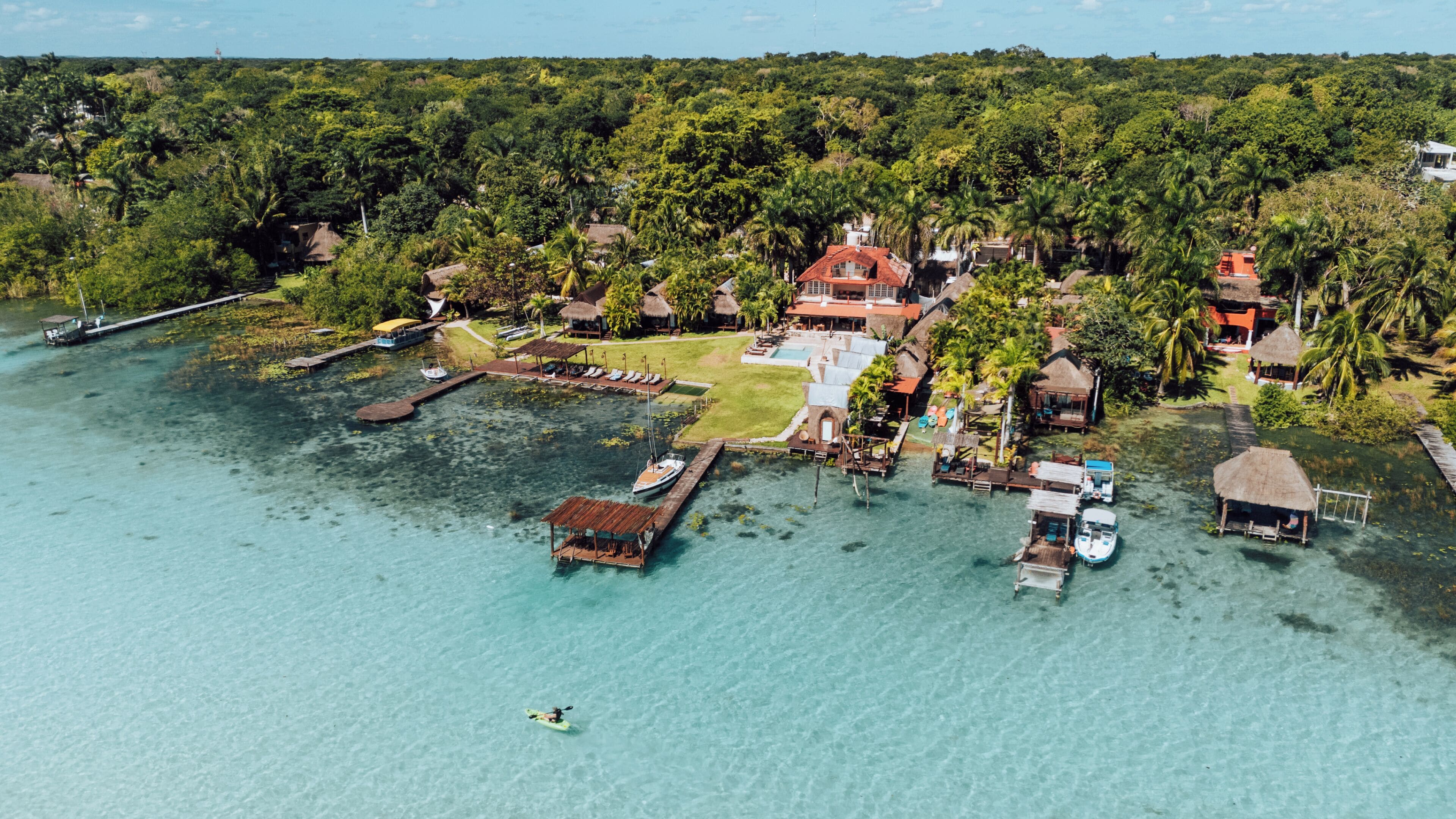 Vista aérea de un resort en una isla tropical con aguas turquesas cristalinas, muelles de madera y estructuras de techo de paja.