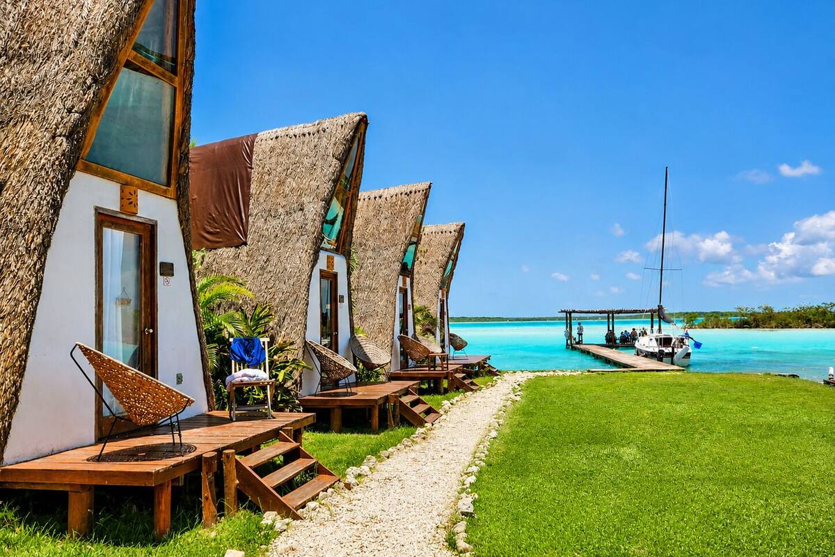 A row of thatched-roof cabins with wooden furniture and a clear view of the turquoise sea.