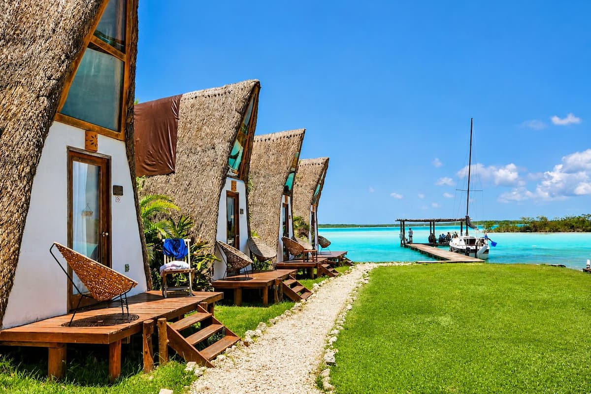 A row of thatched-roof cabins with wooden furniture and a clear view of the turquoise sea.