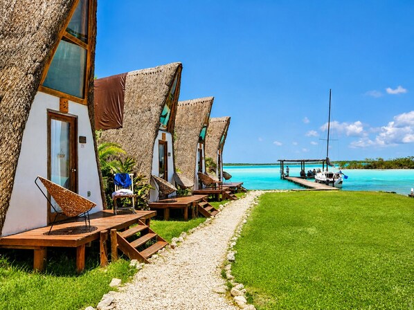 A row of thatched-roof cabins with wooden furniture and a clear view of the turquoise sea.