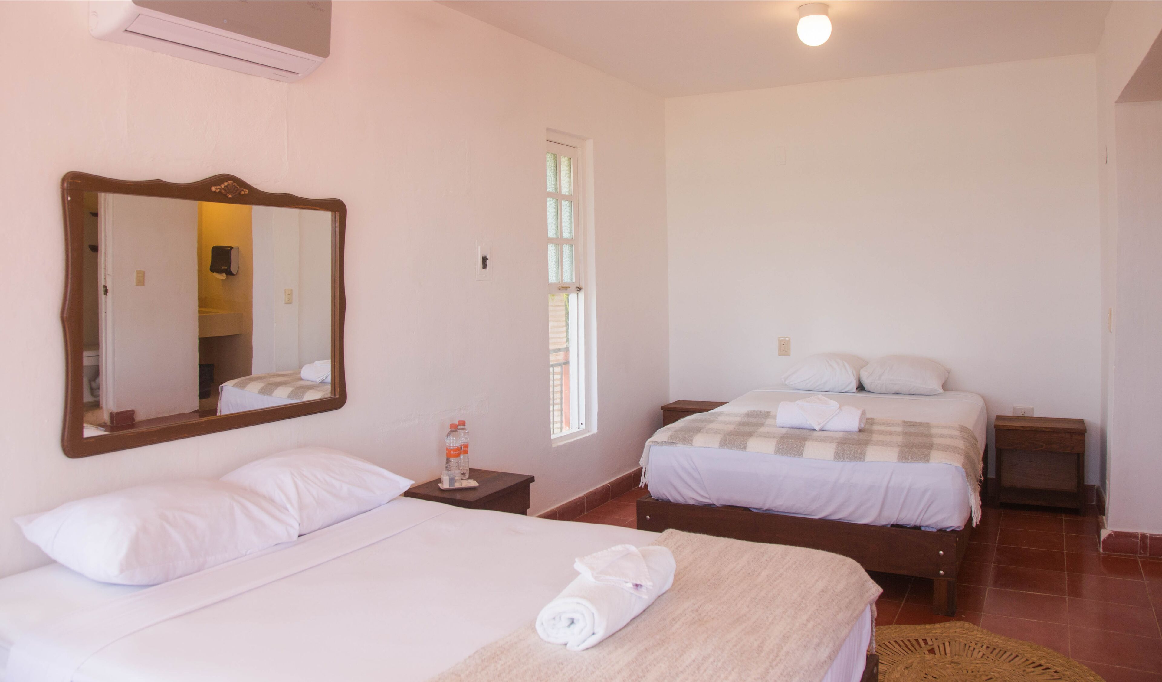 Een hotelkamer met twee bedden, een grote spiegel, een raam en een klein tafeltje met een fles.