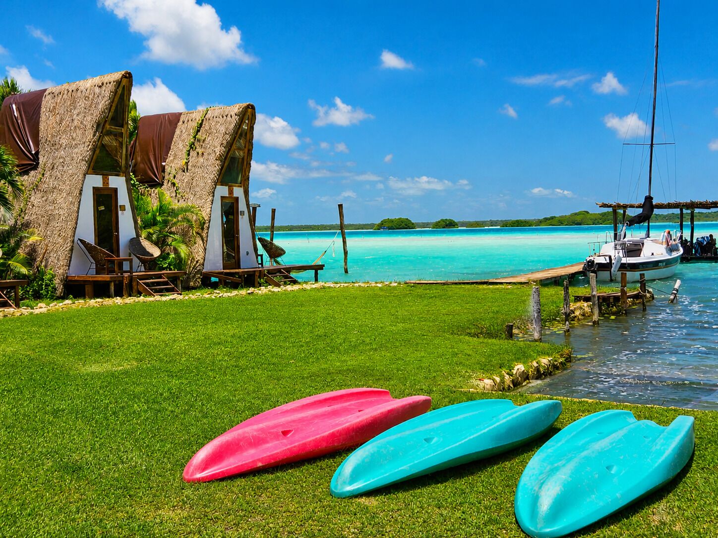 A beachside resort with thatched-roof huts, a grassy lawn, and a clear view of the turquoise sea.