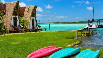 A beachside resort with thatched-roof huts, a grassy lawn, and a clear view of the turquoise sea.