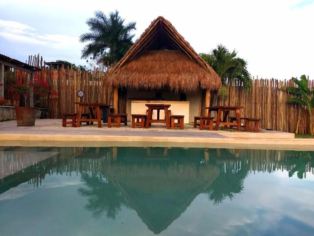 A thatched-roof hut with wooden furniture, a pool, and a bamboo fence.