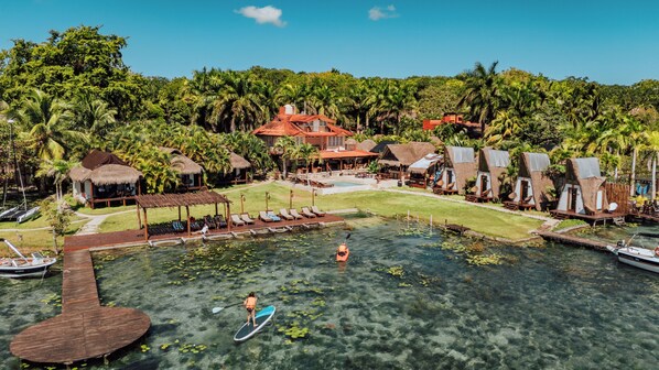 Ein Resort mit einem klaren Pool, Stand-Up-Paddle-Boardern und strohgedeckten Hütten.