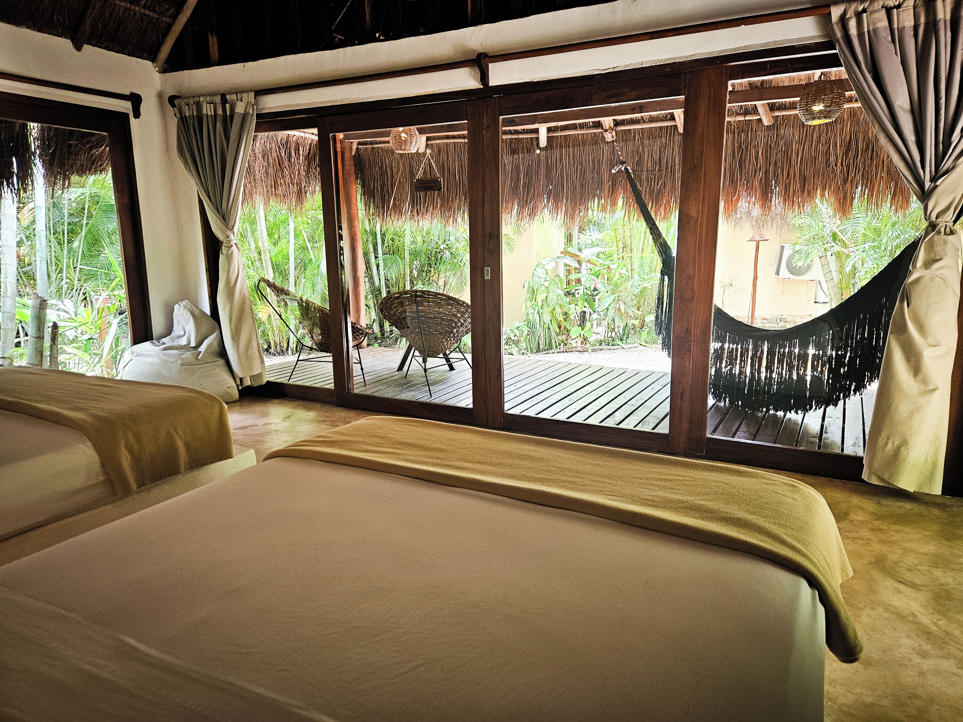 Una habitación con dos camas, una terraza de madera y vistas a la vegetación tropical.