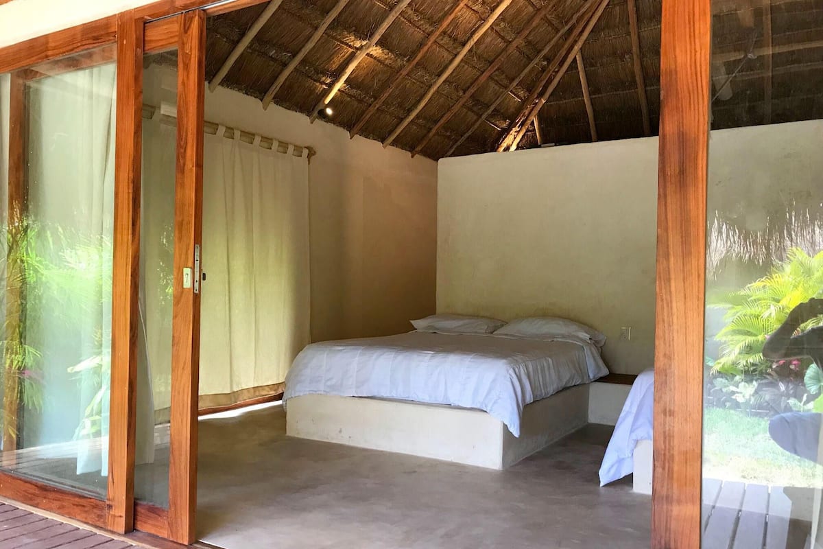 Un dormitorio con cama, puerta corrediza de vidrio y techo de paja.