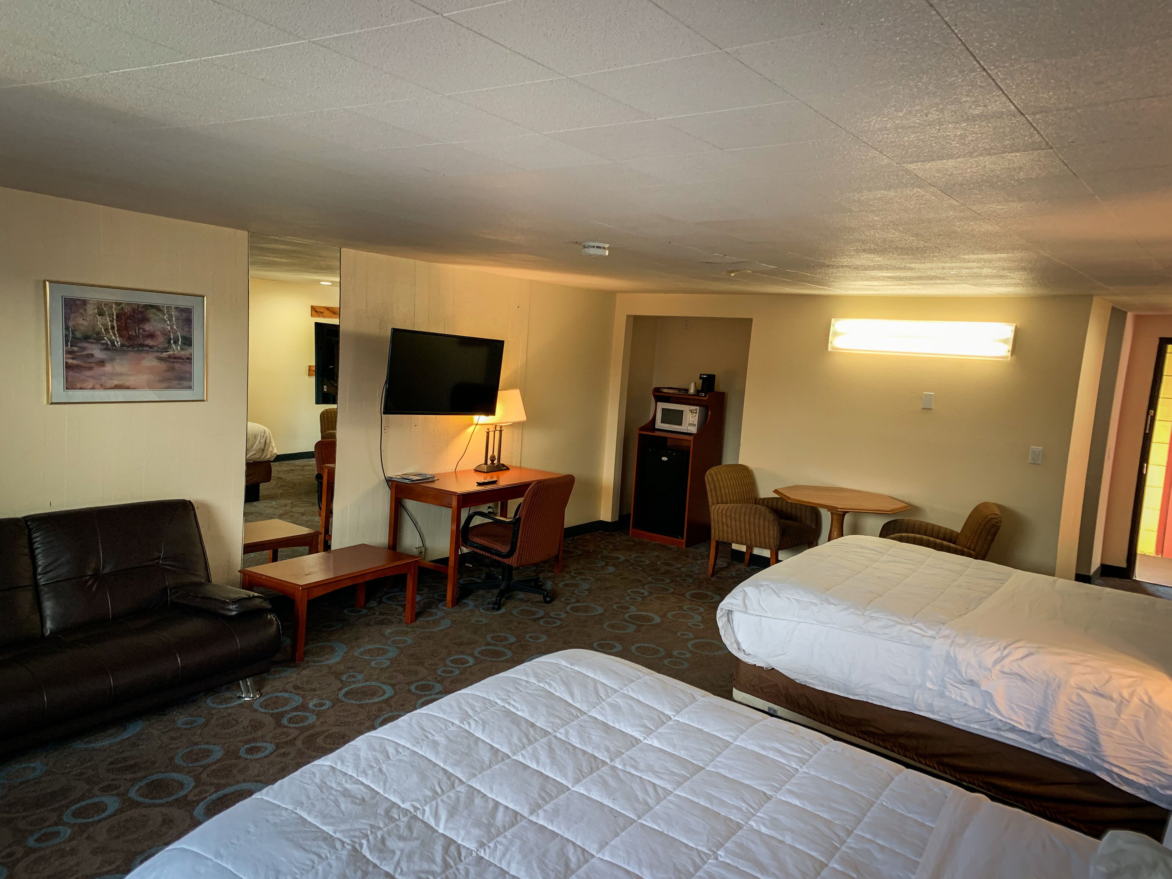 A hotel room with two beds, a desk with a computer, a TV, a microwave, and a seating area with chairs.