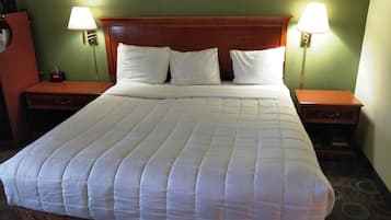 Una cama bien tendida con un cabecero de madera, dos mesitas de noche con lámparas y un reloj en una de ellas.