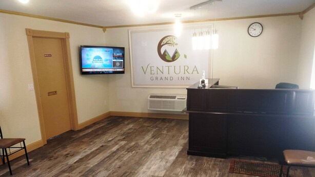 A reception area with a wooden floor, a reception desk, a television, and a clock on the wall. - Ventura Grand Inn (Mammoth Lakes)