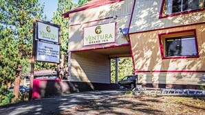 A two-story building with a sign for Ventura Grand Inn, featuring amenities like continental breakfast, DirectTV, Wi-Fi, hot tub, AARP, and pot-friendly facilities. - Ventura Grand Inn (Mammoth Lakes)