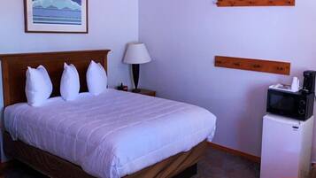 Quarto de hotel com uma cama, mesa de cabeceira, luminária, micro-ondas e uma pequena mesa.