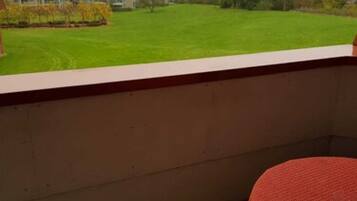 A balcony with a red woven table and a wicker chair.