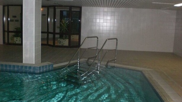 Una piscina interior con agua cristalina, escaleras metálicas y paredes de azulejos.