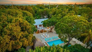 Vista aérea de um resort com piscina, espreguiçadeiras e uma estrutura com telhado de palha.