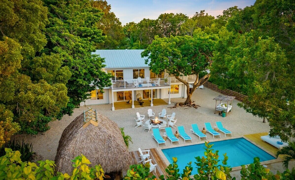 Un bâtiment à deux étages doté d’un balcon, entouré d’arbres, d’une piscine et de chaises longues.