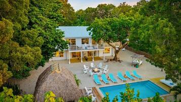 Un bâtiment à deux étages doté d’un balcon, entouré d’arbres, d’une piscine et de chaises longues.