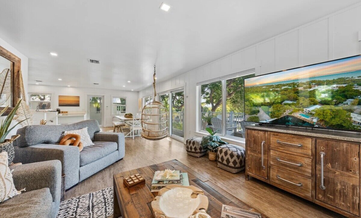 A spacious living room with a large TV, wooden cabinets, and a view of a landscape.