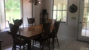 A dining area with a wooden table and chairs, a hanging light fixture, and a door with a clock.