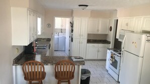 A kitchen with white cabinets, a granite countertop, two wooden bar stools, a trash can, and a stove.