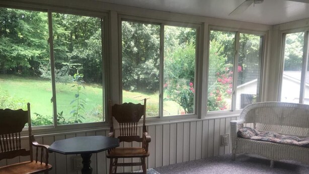 A sunroom with a table and chairs, a wicker sofa, and large windows overlooking a garden.