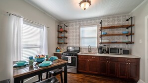 Una cocina con armarios de madera, estufa, microondas y una mesa de comedor con sillas.