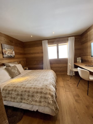 Een knus interieur met houten details, een bed met bloemenbeddengoed, een bureau met stoel en een schilderij van een vos aan de muur.