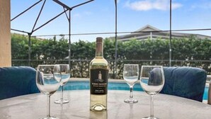 Un tavolo con una bottiglia di vino e due bicchieri, con vista su una piscina e vegetazione.