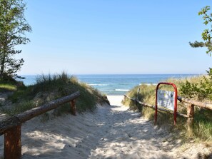 Ein Sandweg am Strand, der zum Meer führt, mit einem Schild, das auf einen geschützten Bereich hinweist.