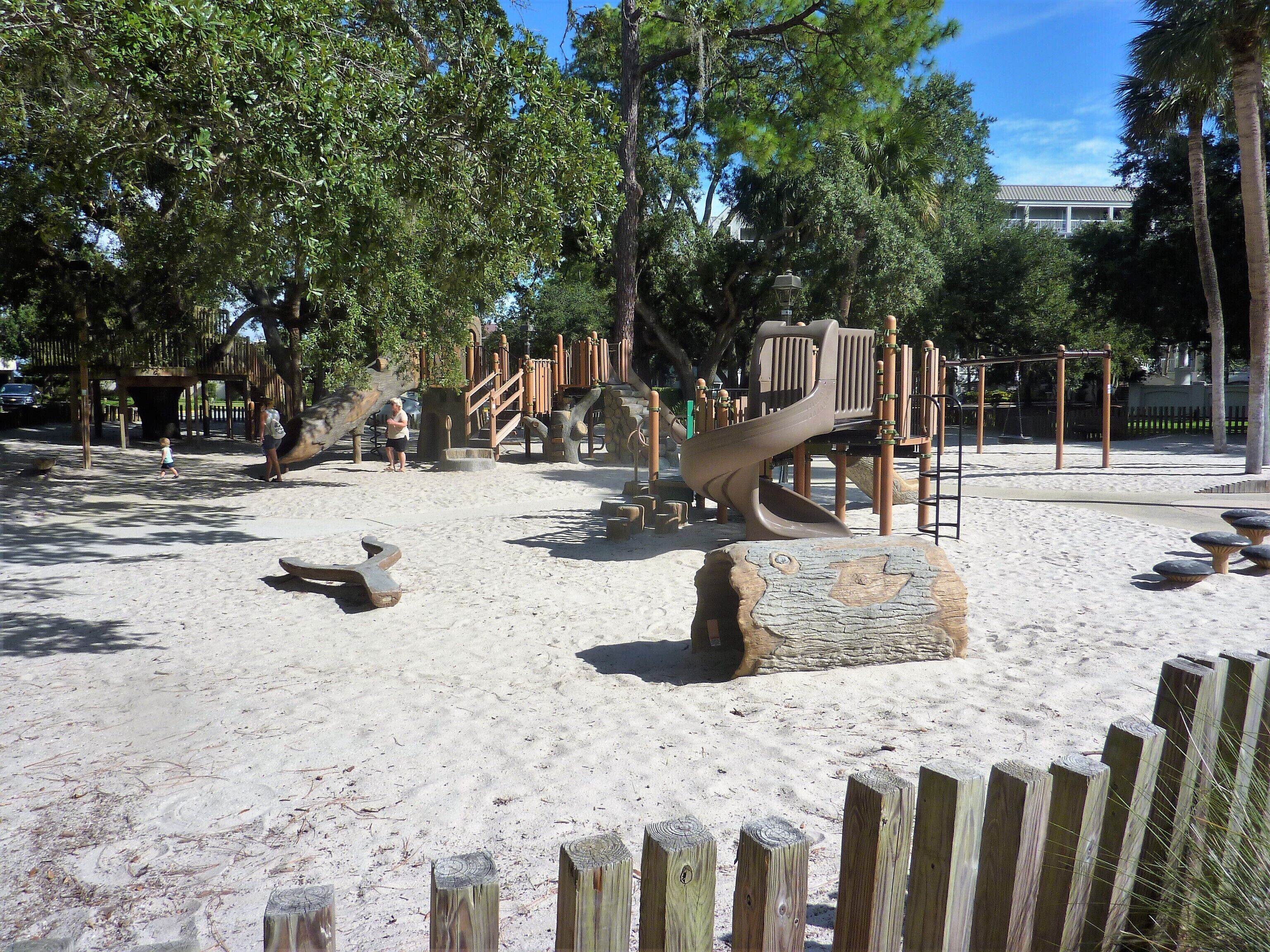 Ein Spielplatz mit Sand, Holzkonstruktionen und Bäumen.