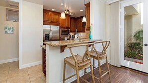 A kitchen with wooden cabinets, a stainless steel refrigerator, an oven, a microwave, and a bar area with two wicker chairs.