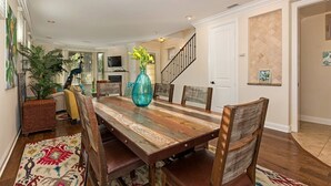 A dining area with a wooden table, chairs, and a vase. There is a staircase and a door in the background.