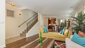 A spacious living room with a wooden coffee table, a yellow sofa with patterned cushions, and a staircase leading to the upper floor.
