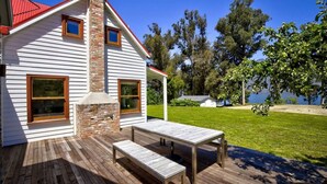 Une maison dotée d’une terrasse en bois, d’une cheminée en pierre et offrant une vue sur un lac.